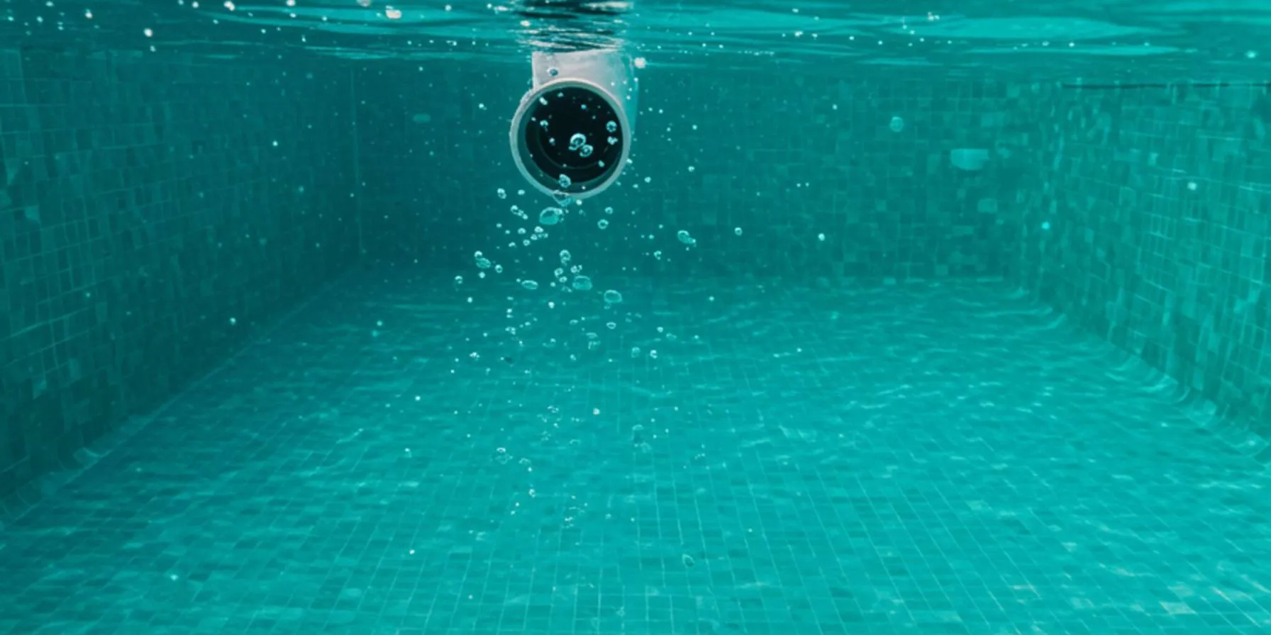 "Perspectiva submarina de una piscina de lujo en una villa andaluza, mostrando burbujas de aire de una fuga en una unión de tubería, mientras un técnico utiliza una cámara digital para detectar fugas."